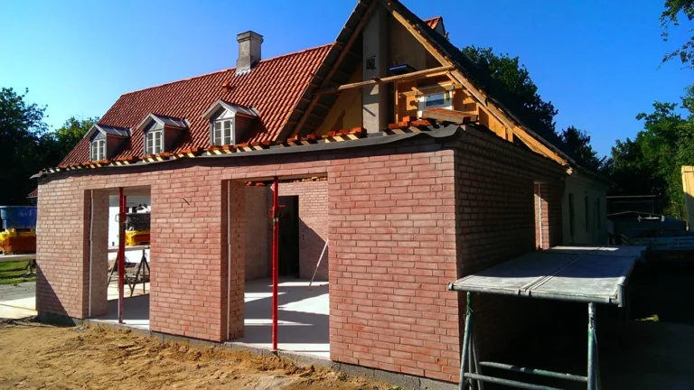 Byggeproces af en tilbygning på Thurø, hvor der er opmuret en rød murstensvæg. Det eksisterende hus med rødt tegltag og tagkviste kan ses i baggrunden.